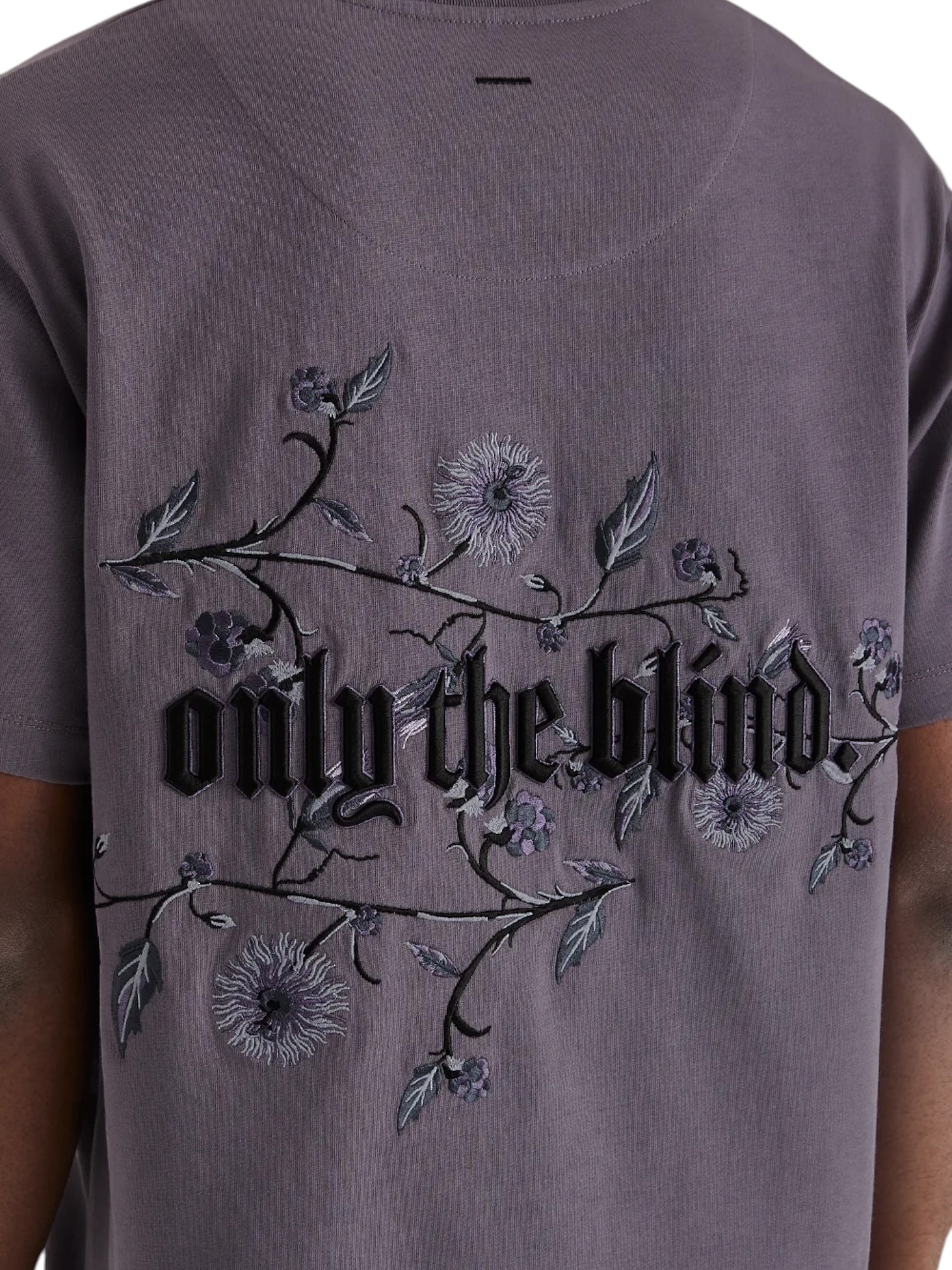 Back view of a person wearing a purple Only The Blind OTB-T1383 Wildflower T-Shirt with intricate blackberry floral embroidery and "only the blind" text.
