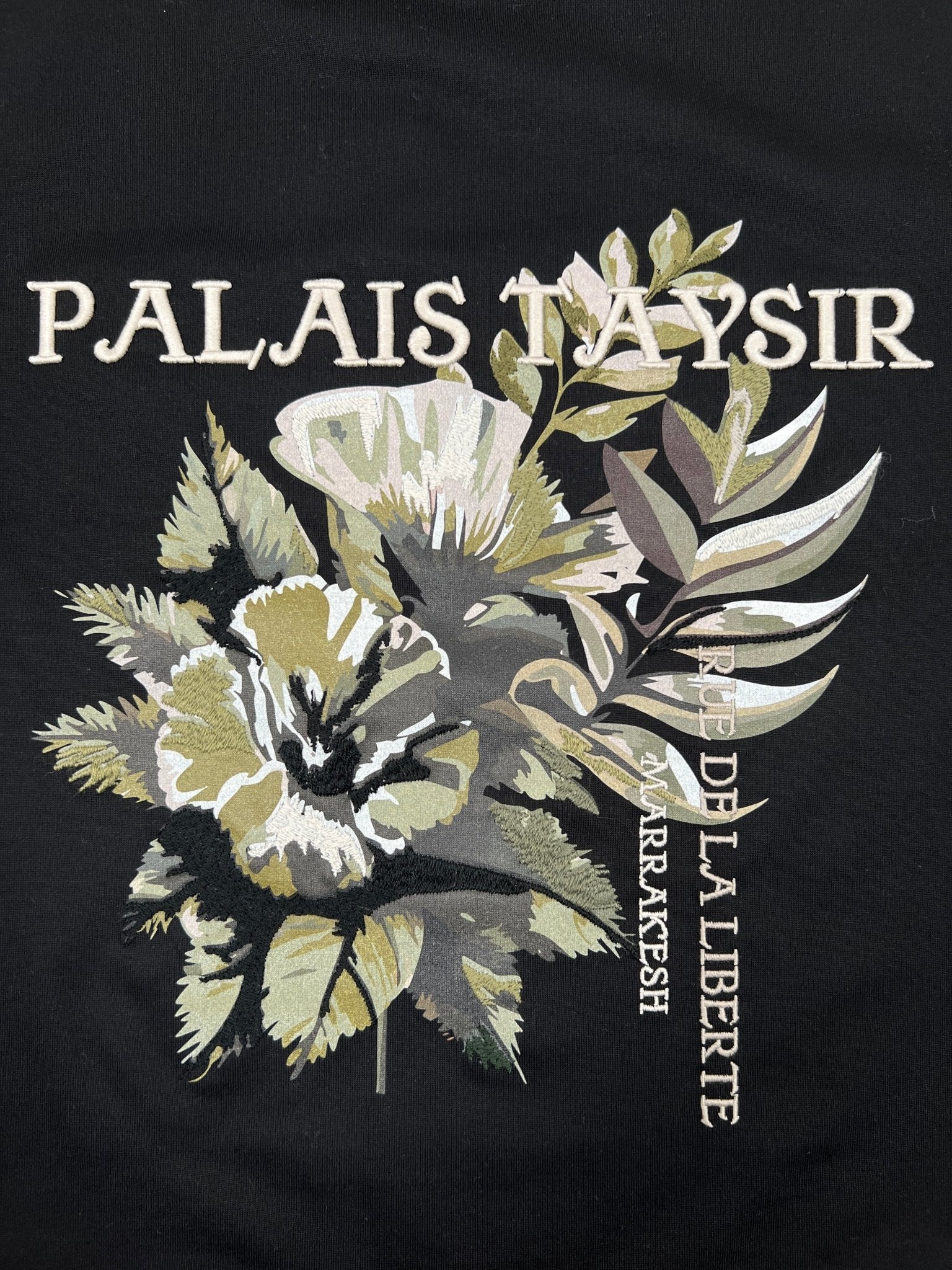 The Only The Blind OTB-T1472 Botanical T-shirt features an embroidered floral graphic with "PALACE TAYSIR" and "RUE DE LA LIBERTE MARRAKESH" text on black organic cotton.
