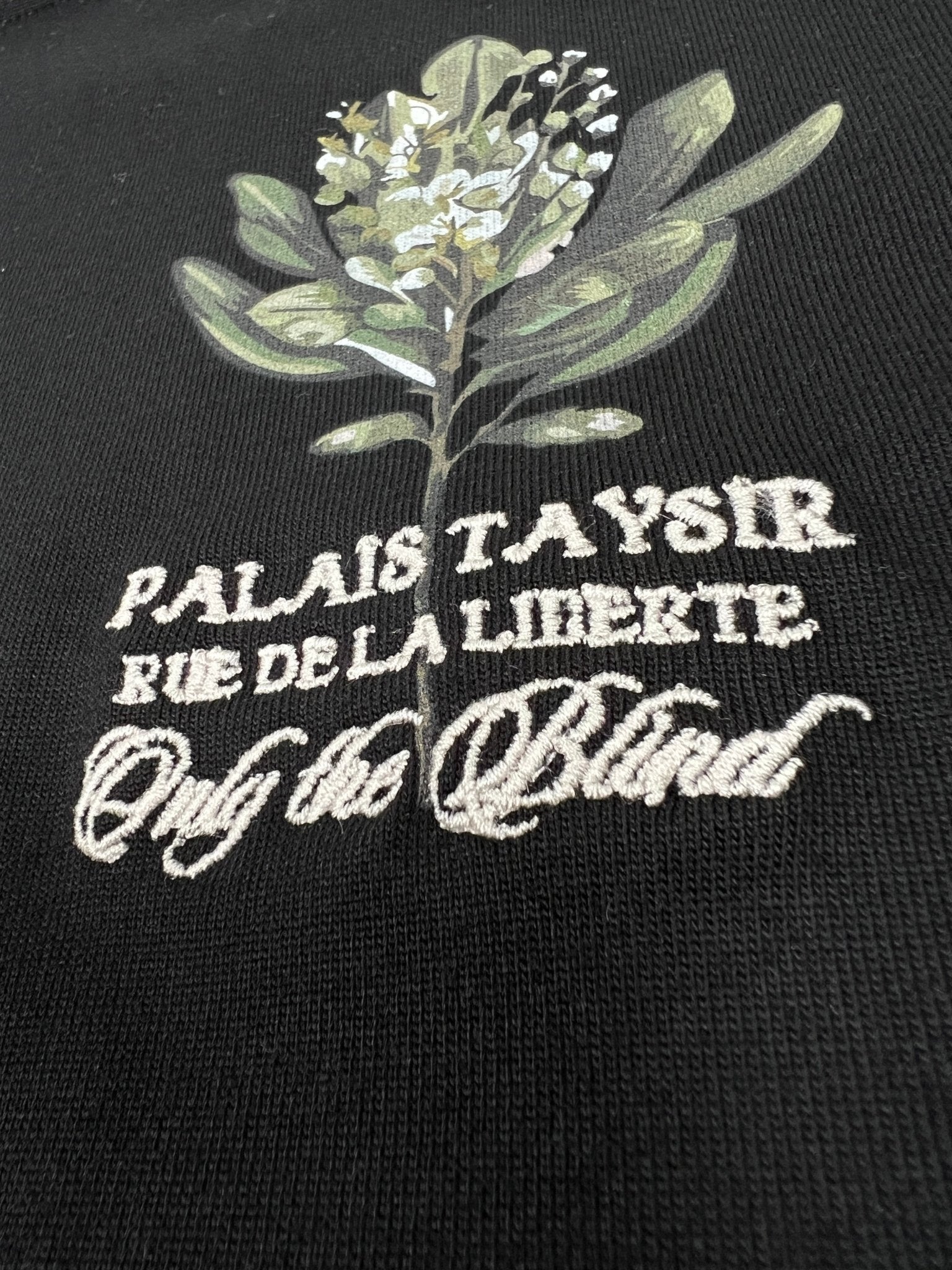 The Only The Blind OTB-T1472 Botanical T-shirt in black features an embroidered flower design on organic cotton, with the text: "PALAIS TAYSIR RUE DE LA LIBERTE Only the Blind.