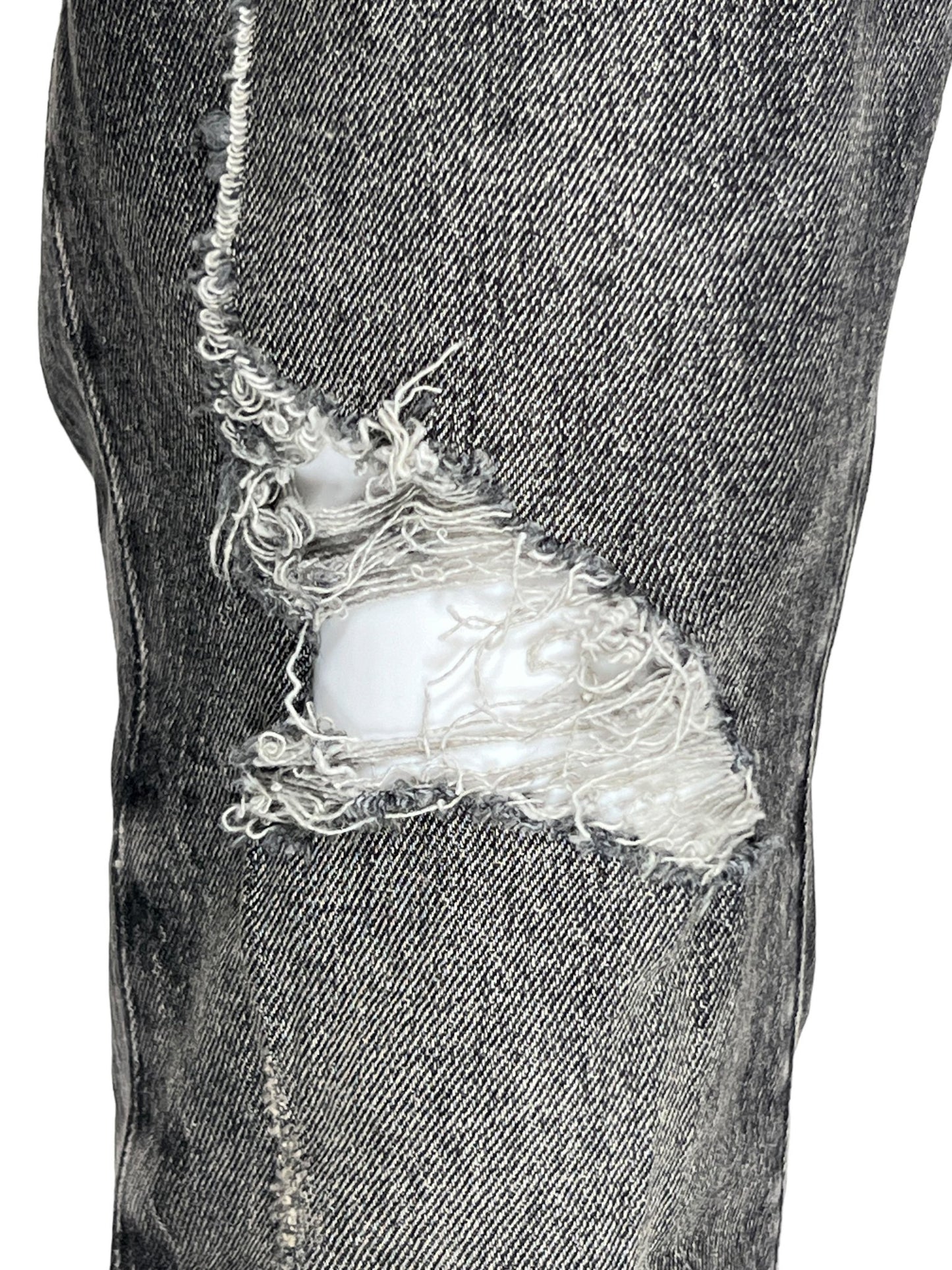 Close-up of a pair of P001-SWKO SKINNY WEEK OLD WASH BLACK jeans from PURPLE BRAND, featuring a faded dark grey color with a prominent frayed hole at the knee, revealing white cotton fabric underneath.