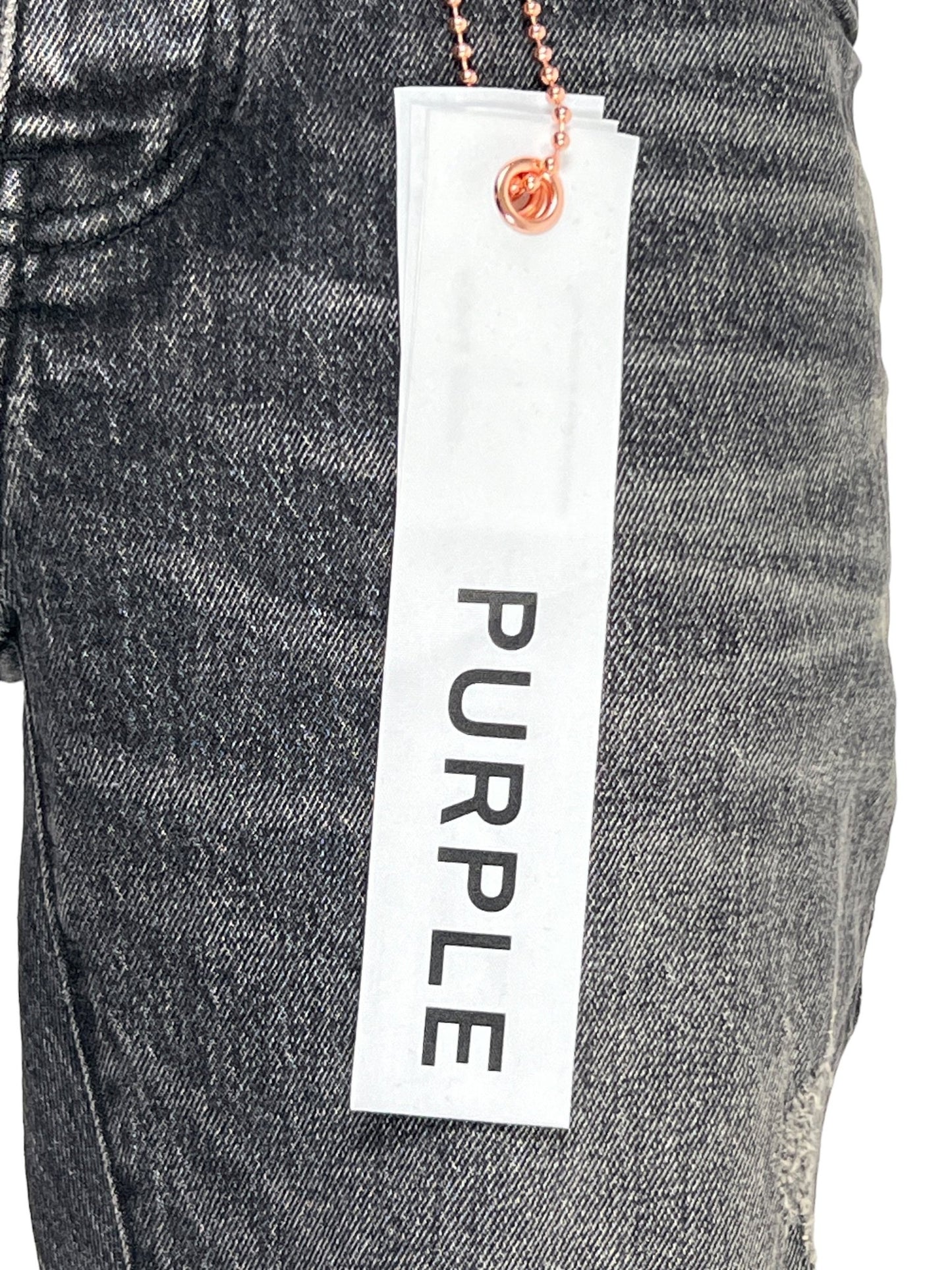 Close-up of a faded dark grey ripped jean fabric from PURPLE BRAND's P001-SWKO SKINNY WEEK OLD WASH BLACK collection, featuring a white tag with the brand name "PURPLE" attached by a ball chain.