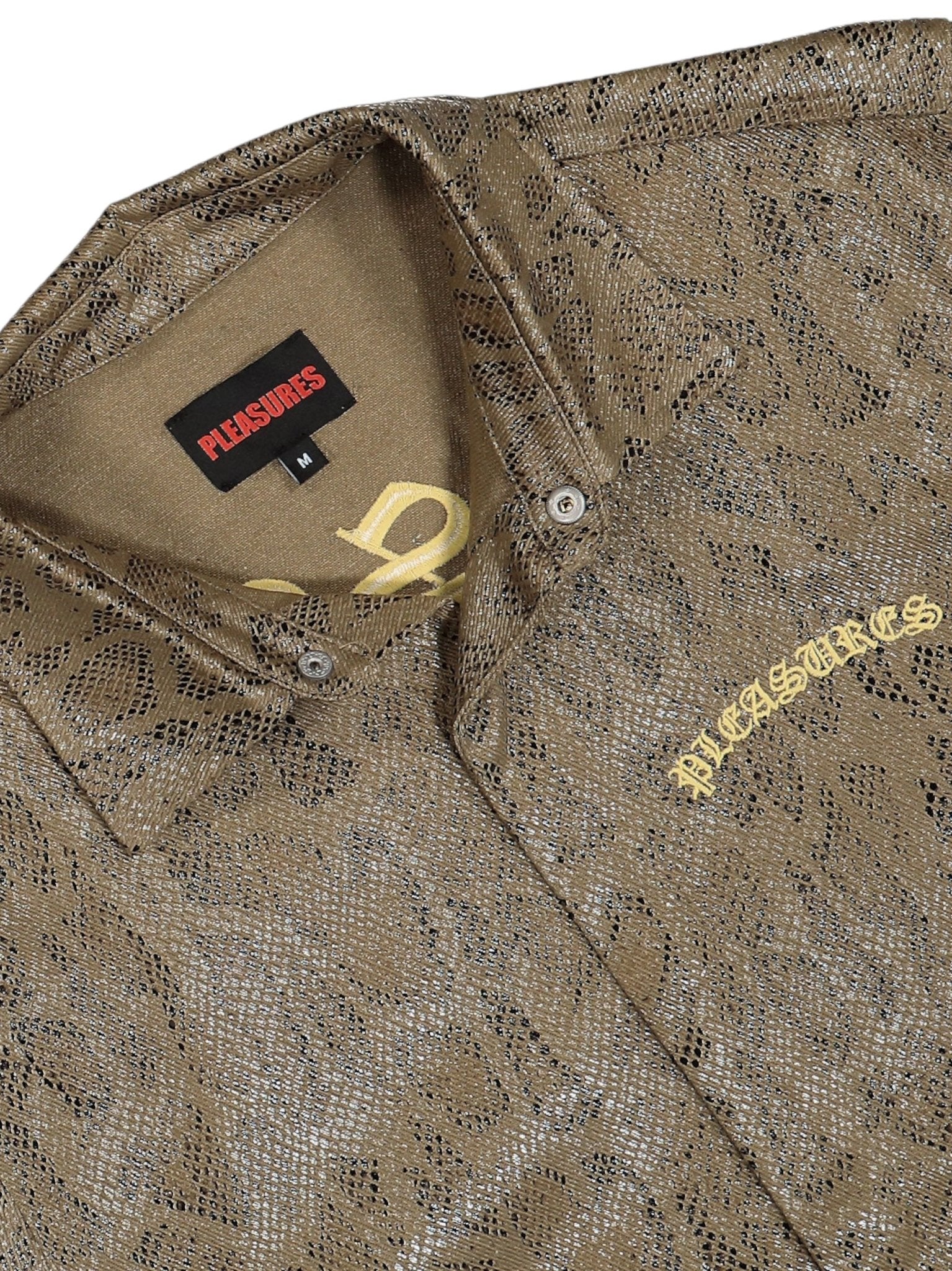 Close-up of the brown Pleasures Anaconda Overshirt Brw, highlighting its textured pattern with "PLEASURES" in yellow on the chest and a small collar tag.