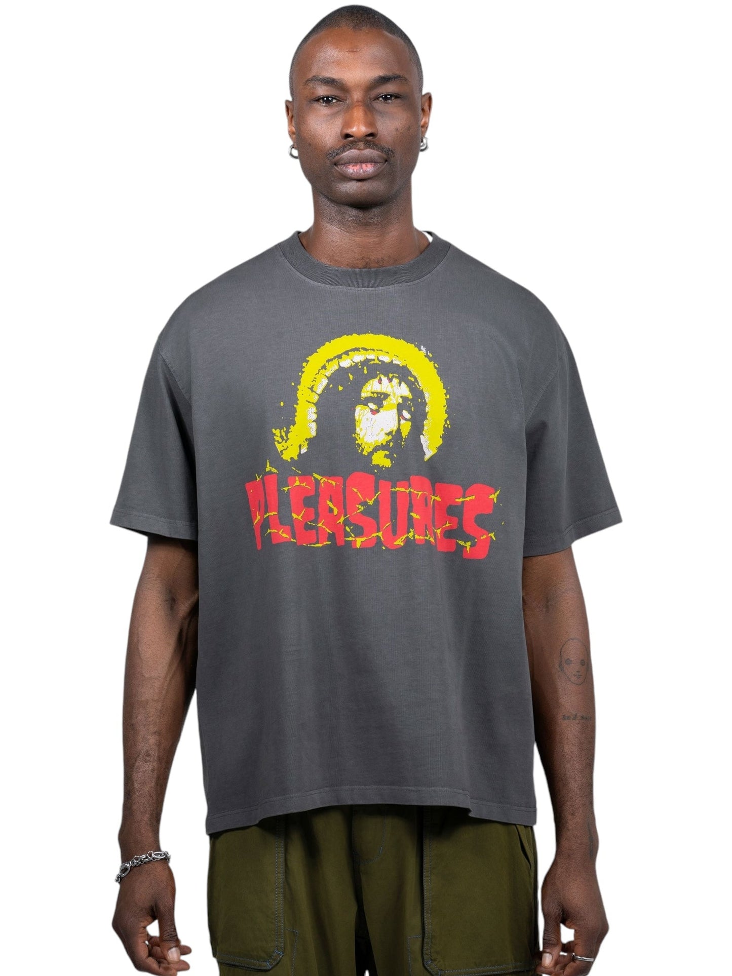 Someone stands against a white background wearing a black Pleasures Chosen heavyweight shirt by PLEASURES, featuring a graphic on the front and paired with green pants. Its boxy fit and cotton jersey fabric ensure added comfort.