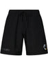 The Pleasures Crush Hiking Shorts Black by PLEASURES are nylon shorts with an elastic waistband, "PLEASURES" text on the left leg, and a small helmet graphic on the lower right leg.