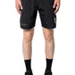 Someone stands against a plain background wearing PLEASURES Crush Hiking Shorts Black—nylon shorts with an elasticized waistband and small graphic on one leg—paired with black socks and sneakers.