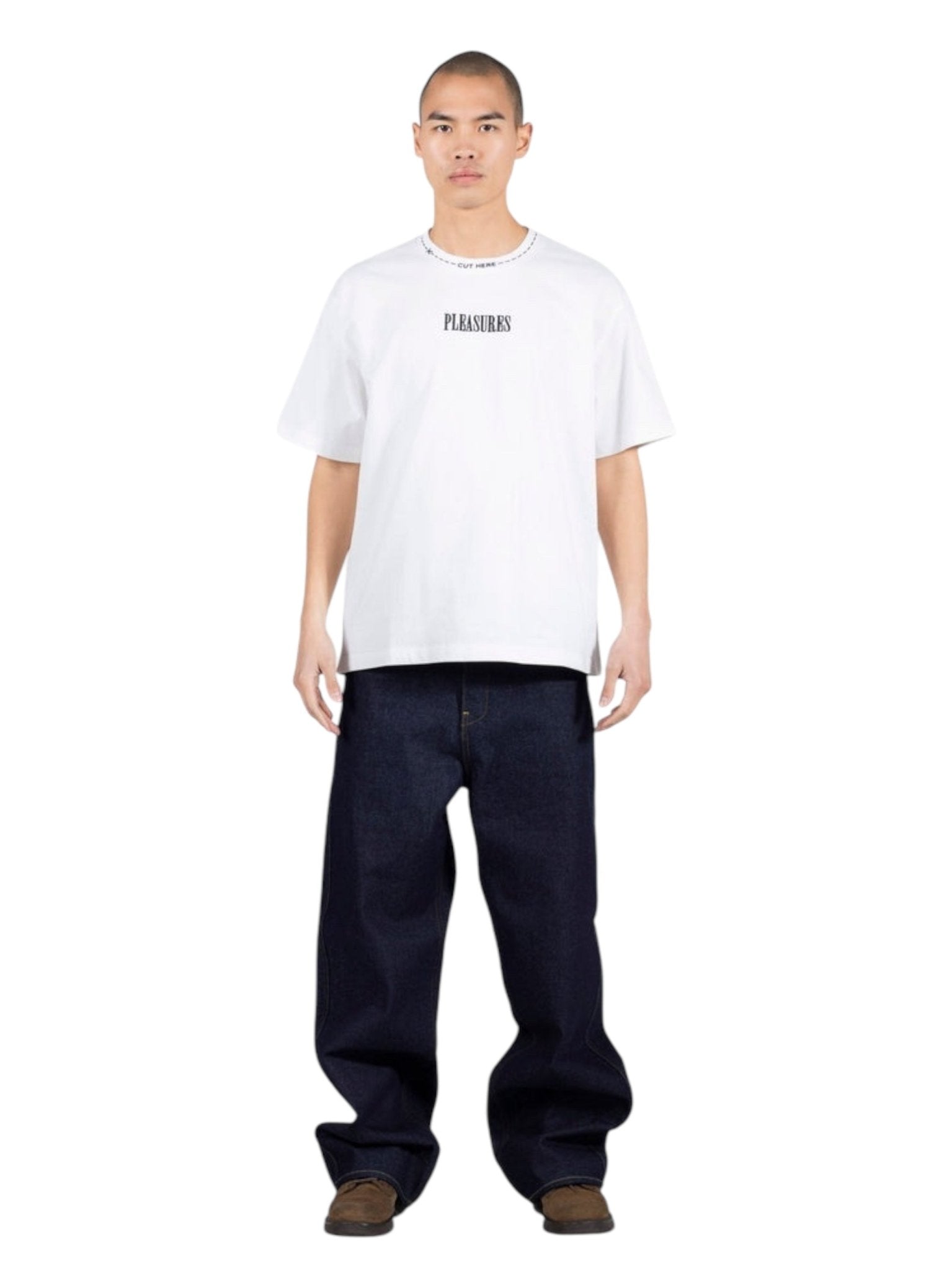 A person stands facing forward in a Pleasures Cut Here Heavyweight T-Shirt Wht by PLEASURES, styled with loose dark blue jeans and brown shoes, all set against a plain white background.