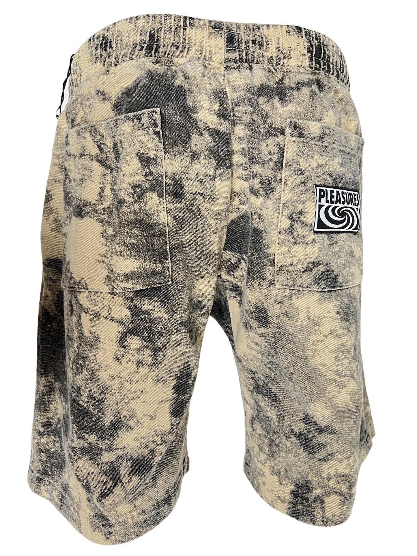 A pair of beige and black PLEASURES CYCLONE SHORTS BLACK with an elastic waistband and two large back pockets crafted from 100% cotton. One pocket features a patch with the brand name "Pleasures" and a wave logo.