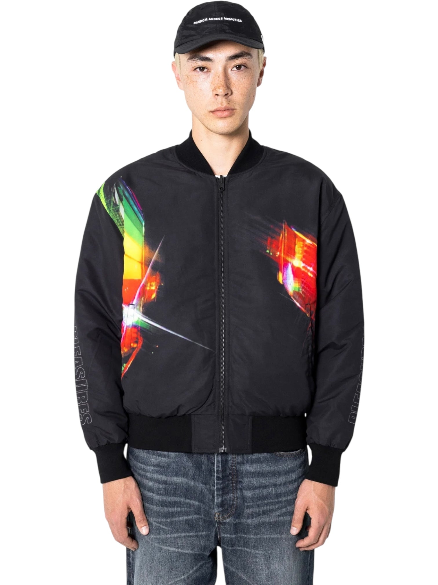 A person wearing a black cap, blue jeans, and the PLEASURES Daft Club Reversible Bomber in black stands facing forward against a plain background.