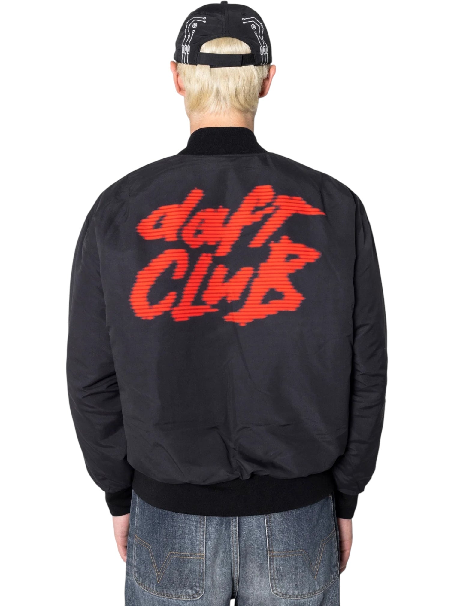 Person seen from behind wearing the PLEASURES Daft Club Reversible Bomber Black, a padded Taslan nylon jacket with "daft CLUB" in red stylized graphics on the back.