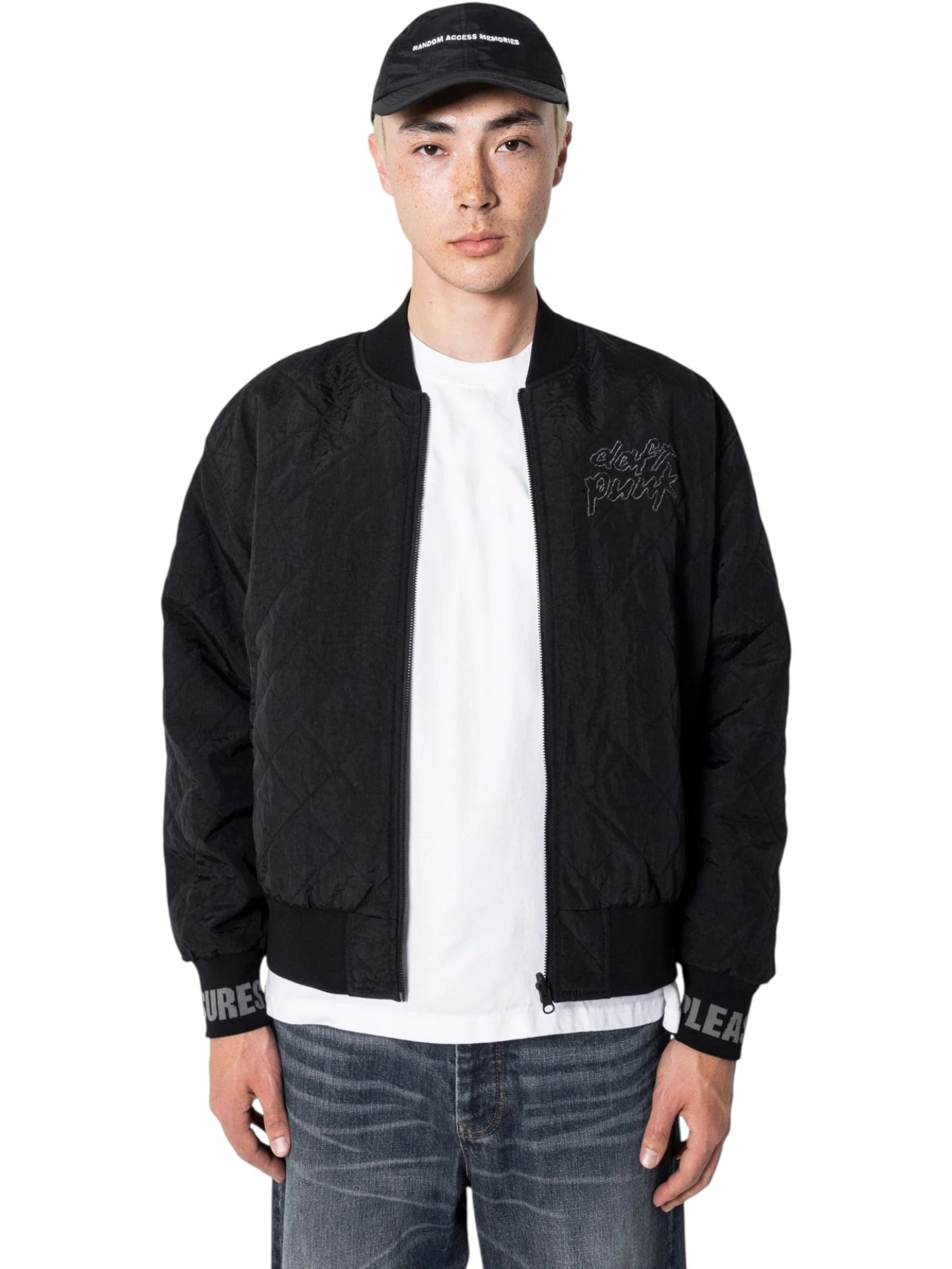 A person stands facing forward wearing the PLEASURES Daft Club Reversible Bomber Black over a white t-shirt, blue jeans, and a black cap with white text.