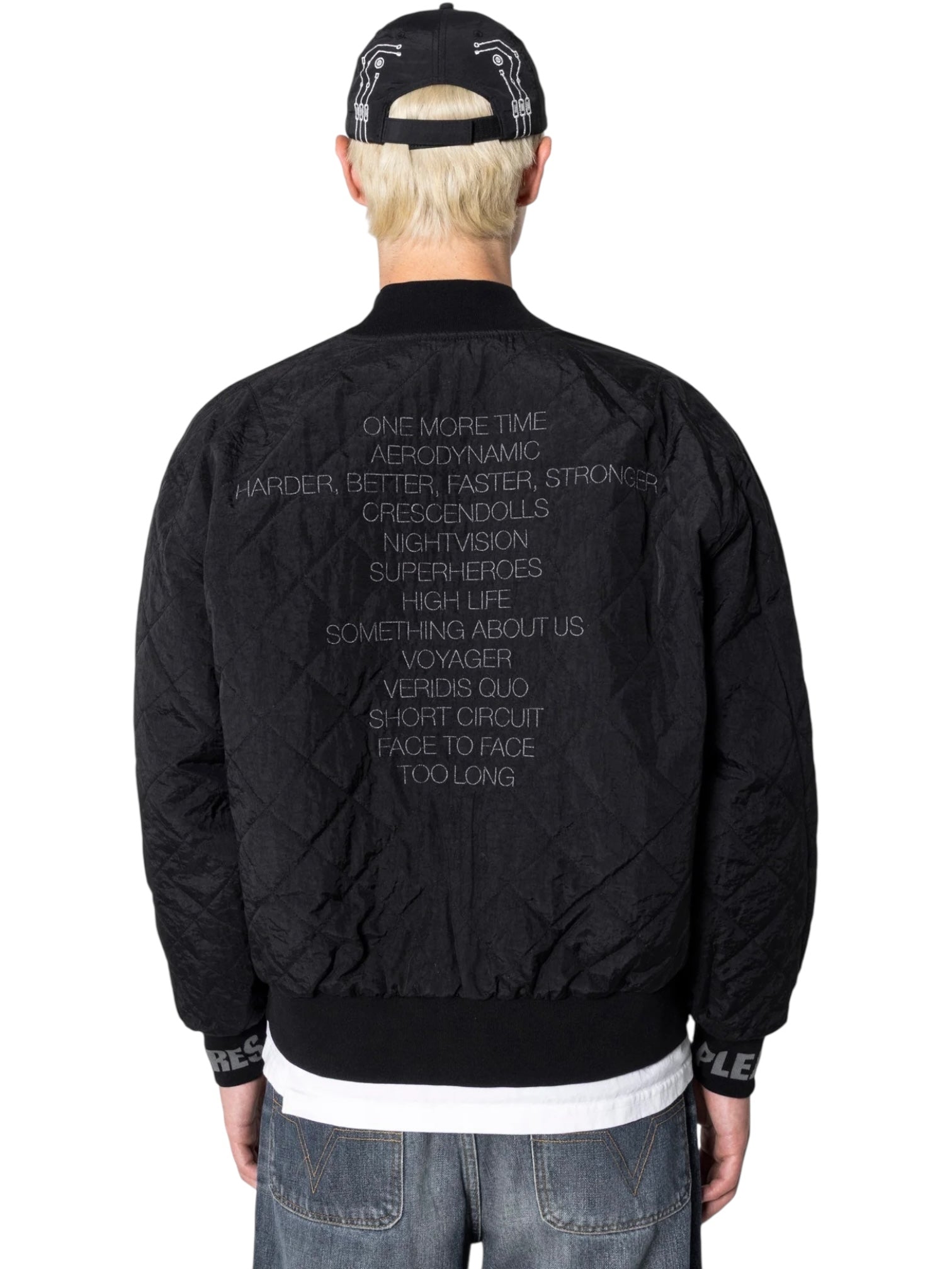 A person wearing the PLEASURES Daft Club Reversible Bomber Black jacket with a list of words on the back and a black cap, shown from behind.