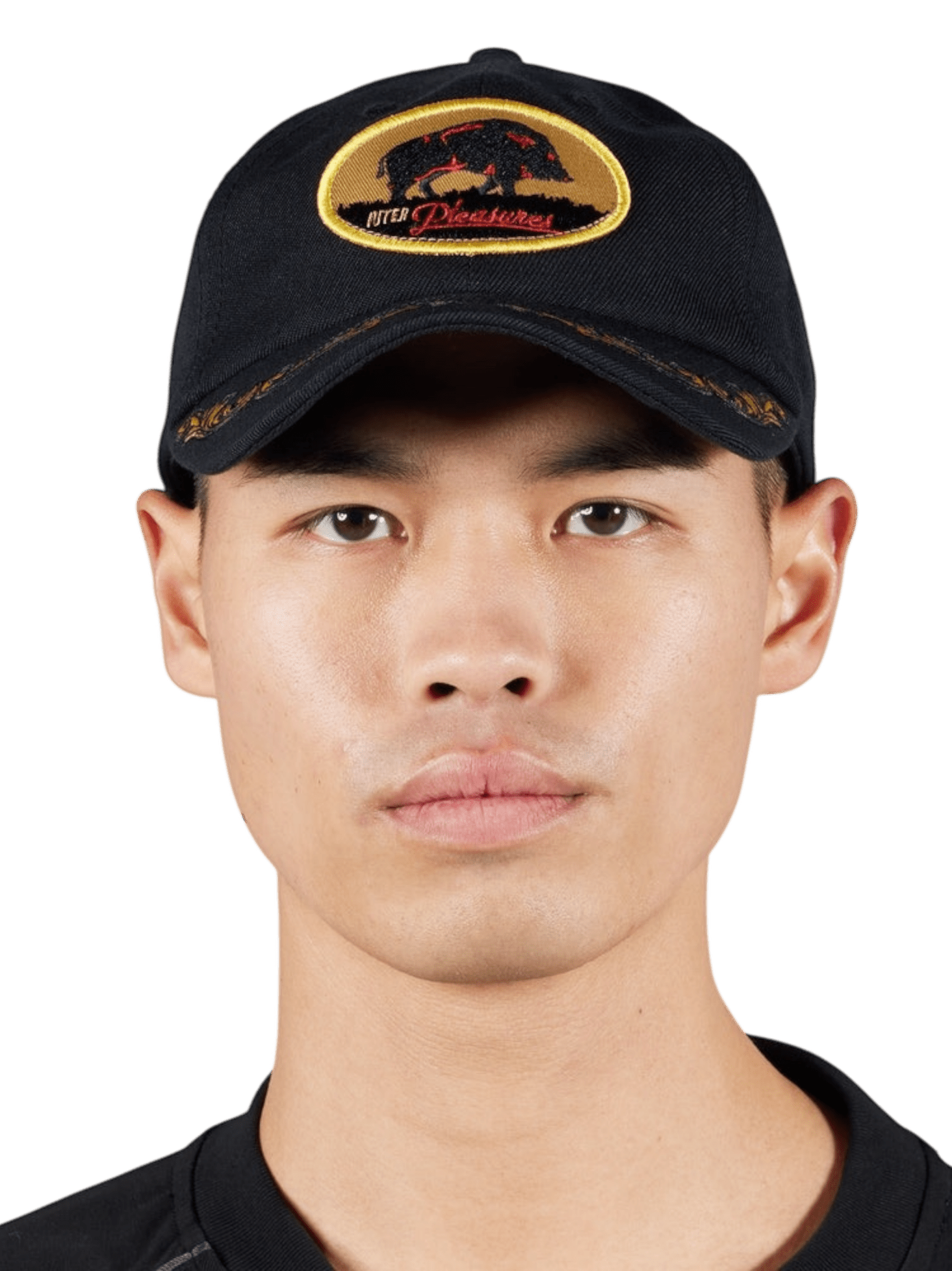 A person wearing the Pleasures Daniele Cap Black, adorned with a yellow and red embroidered boar logo, stands against a plain background. This PLEASURES cap from the Pleasures x Iuter collaboration offers an adjustable fit for comfort and unique flair.