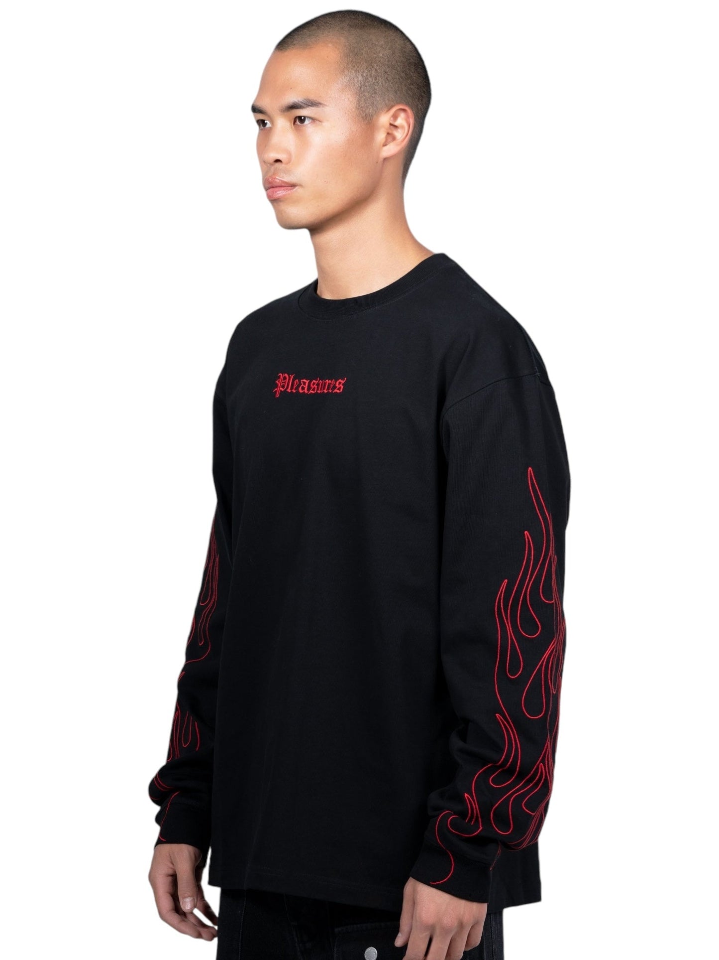 A person is wearing a Pleasures Fiery Heavyweight L/S T-shirt in black by PLEASURES, featuring red graphic text on the front and flames on the arms.