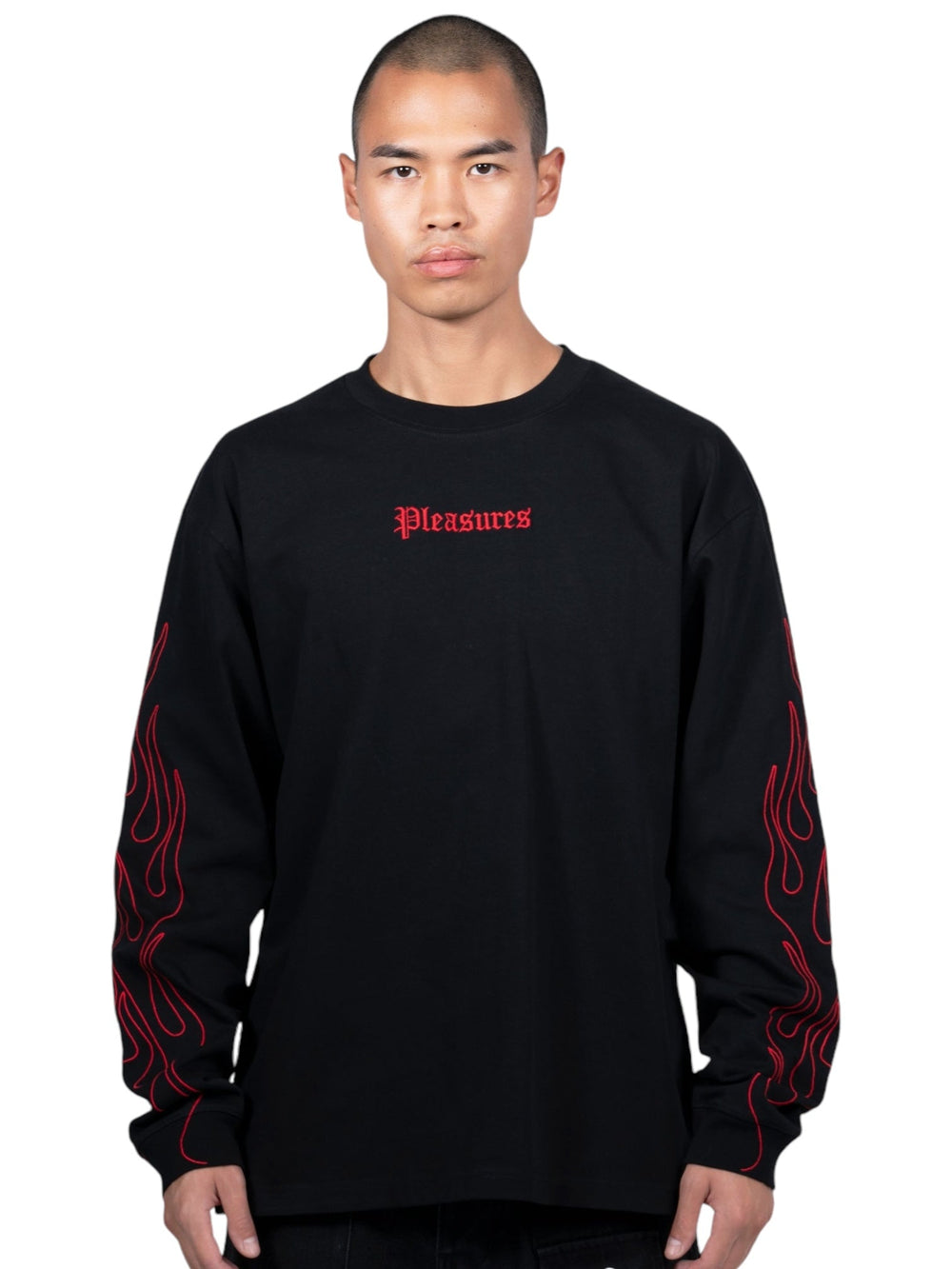 A person wearing the Pleasures Fiery Heavyweight L/S T-shirt in Black, by PLEASURES, shows an embroidered "Pleasures" logo in red on the chest and vivid red flames down the arms.