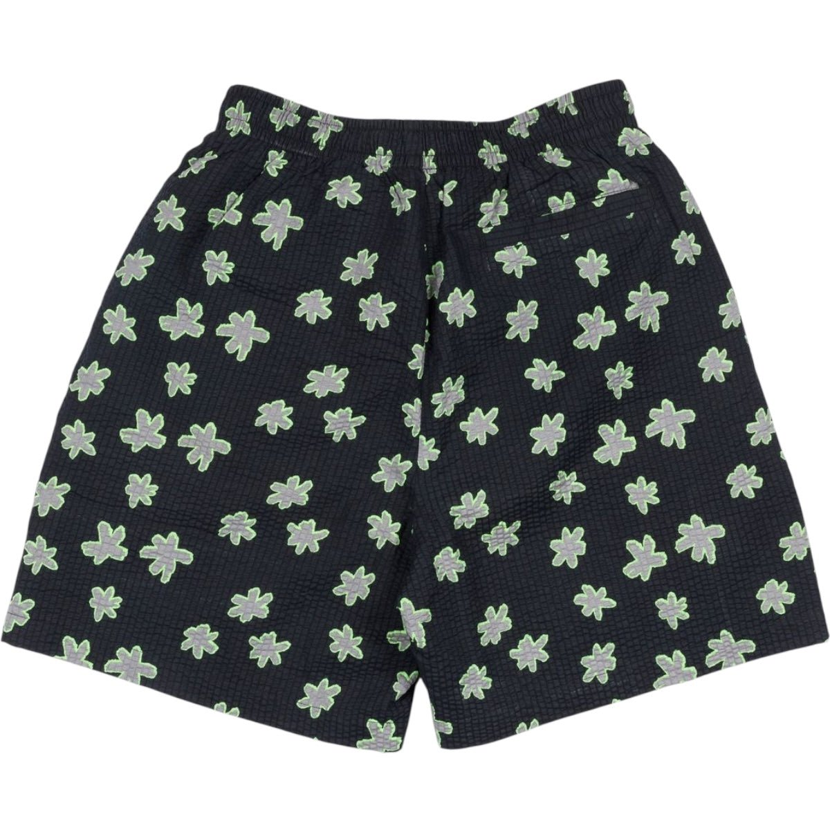 The Pleasures Floral Seersucker Shorts Black by PLEASURES feature black cotton seersucker fabric, an elastic waistband, green and white floral pattern, a single buttoned back pocket, and an embroidered logo.
