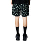 Someone wearing PLEASURES Pleasures Floral Seersucker Shorts Black with a green four-leaf clover pattern, paired with black socks and shoes, photographed from behind against a white background.