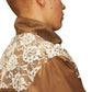 A person with short hair wears the Pleasures Francesca Track Jkt Brown by PLEASURES, a chic brown jacket made from Polyamide, featuring an elegant white floral lace design on the shoulder and back, embodying Italian craftsmanship.