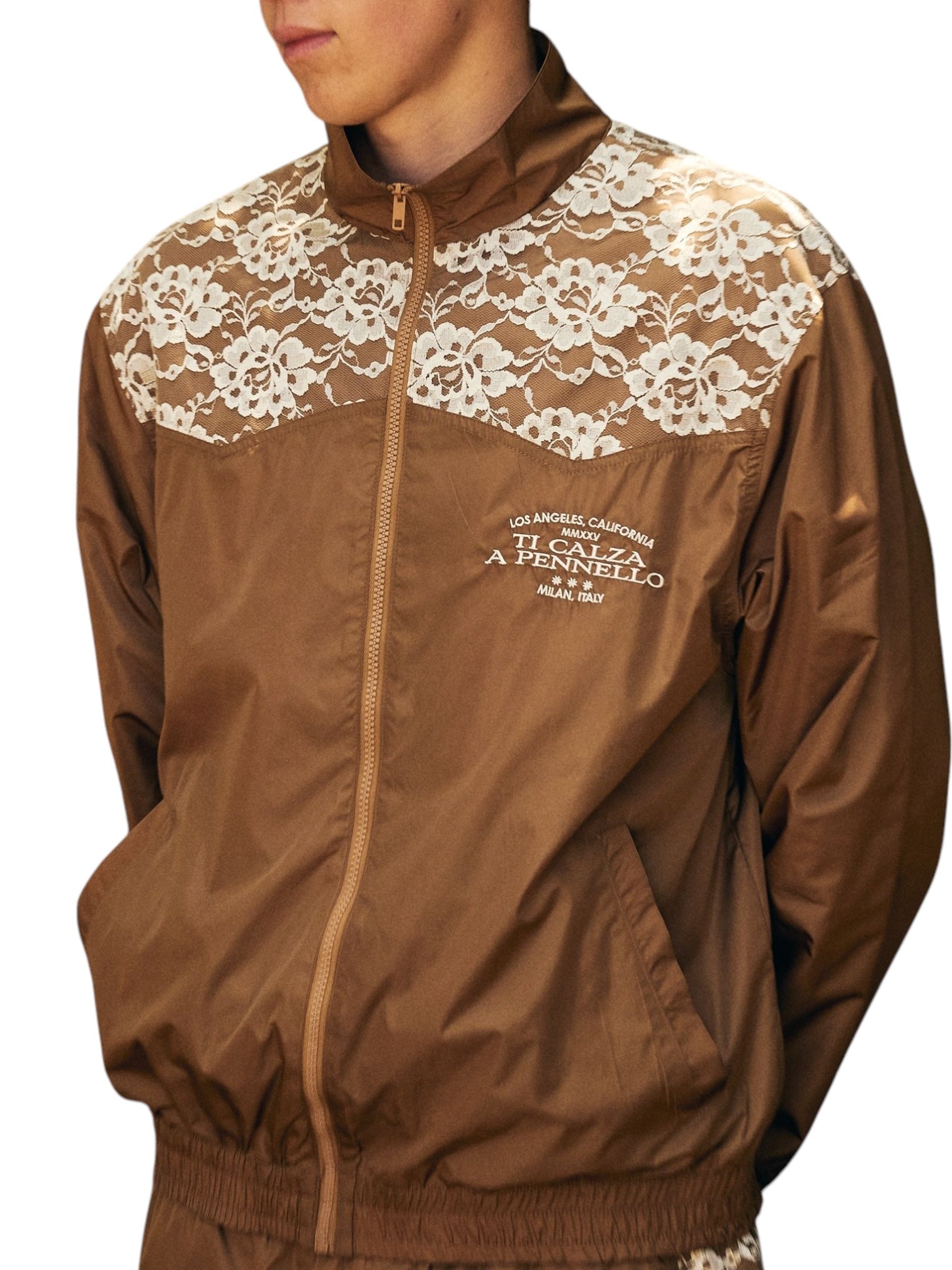 Dressed in a Pleasures Francesca Track Jkt Brown, adorned with white lace on the shoulders and subtle text on the chest, this polyamide-made piece from PLEASURES effortlessly combines casual elegance and distinctive flair.