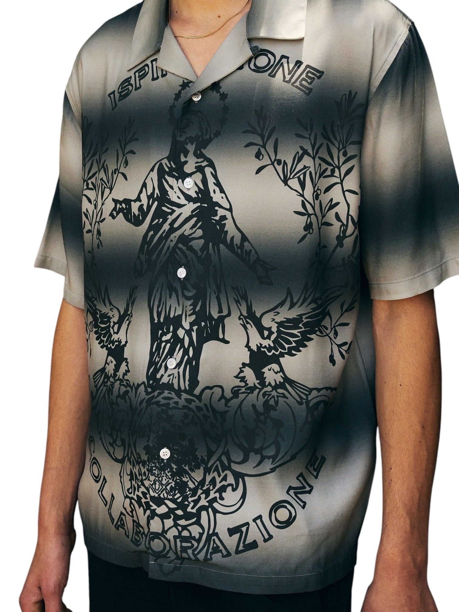 A person is wearing the Pleasures Giovanni BUTTON UP SILVER shirt by PLEASURES. It features a monochrome graphic with a statue, birds, and "Ispirazione Collaborazione," crafted from luxurious Viscose Challis. This stylish short-sleeve shirt also boasts a classic camp collar for added flair.