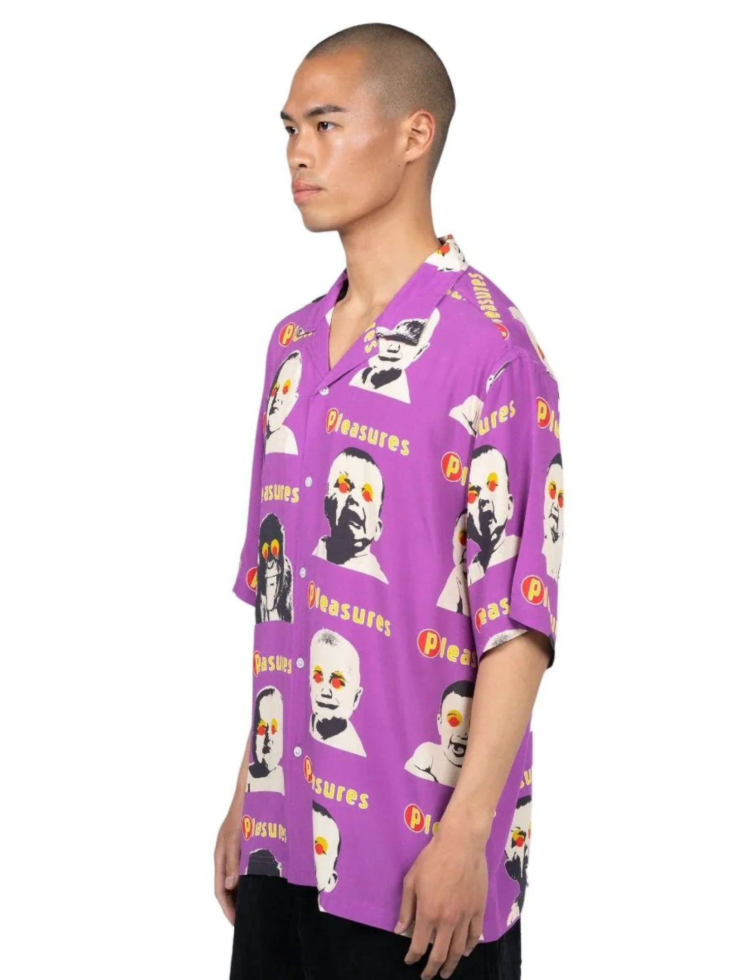 A person stands in profile wearing a bright purple button-down PLEASURES HEAD BUTTON DOWN PURPLE shirt by PLEASURES, featuring various images of Albert Einstein and the word "Pleasures" repeated across the luxurious Rayon fabric.