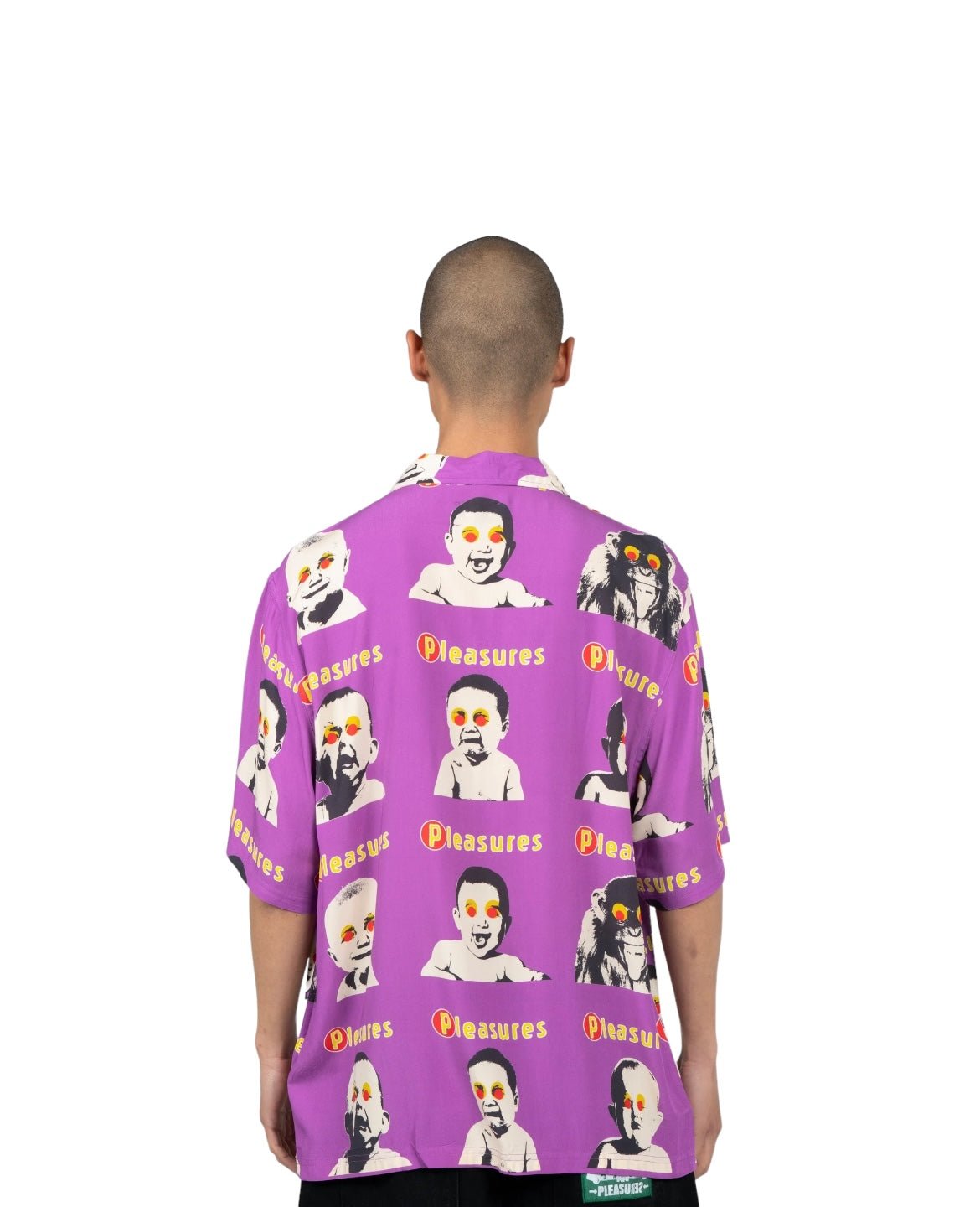 A person with a shaved head wears a PLEASURES HEAD BUTTON DOWN PURPLE featuring various cartoon faces and the word "PLEASURES." The person is shown from the back against a plain white background.