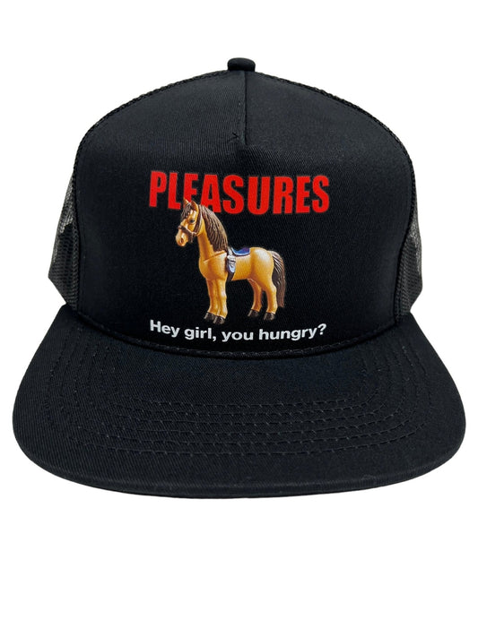 The PLEASURES HORSE TRUCKER BLACK is a black polyester trucker hat featuring the brand name "PLEASURES" in red, accompanied by an image of a toy horse below it and the phrase "Hey girl, you hungry?" written in white.
