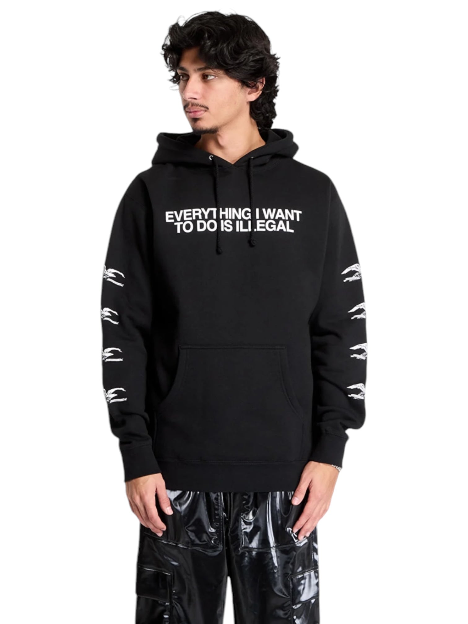 A person is wearing the Pleasures Illegal Hoodie Black by PLEASURES, featuring soft cotton material and "EVERYTHING I WANT TO DO IS ILLEGAL" text on the front. They have their hands in their pockets and are looking to the side.