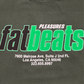 The PLEASURES Melrose T-shirt Ivy is a dark 100% cotton tee featuring "PLEASURES fatbeats" plus the Fat Beats LA address and phone number printed in white and green text.