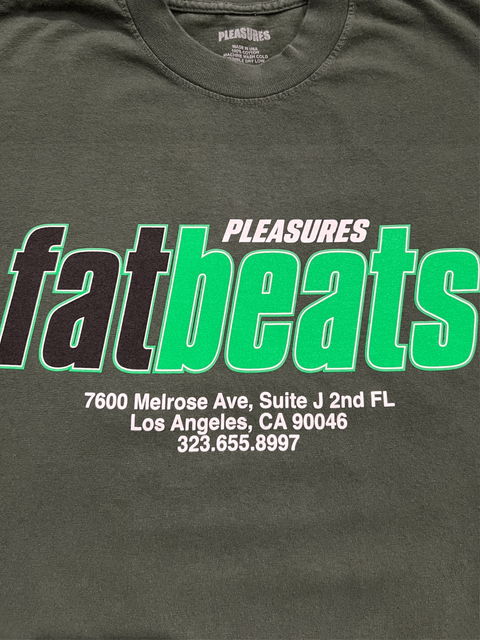 The PLEASURES Melrose T-shirt Ivy is a dark 100% cotton tee featuring "PLEASURES fatbeats" plus the Fat Beats LA address and phone number printed in white and green text.