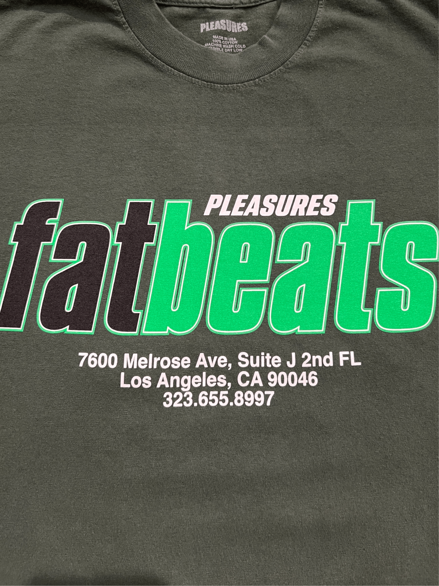 The Pleasures Melrose T-shirt Ivy by PLEASURES is a dark, 100% cotton tee featuring "PLEASURES Fat Beats" and the Melrose Ave address printed on the front. Made in the USA.