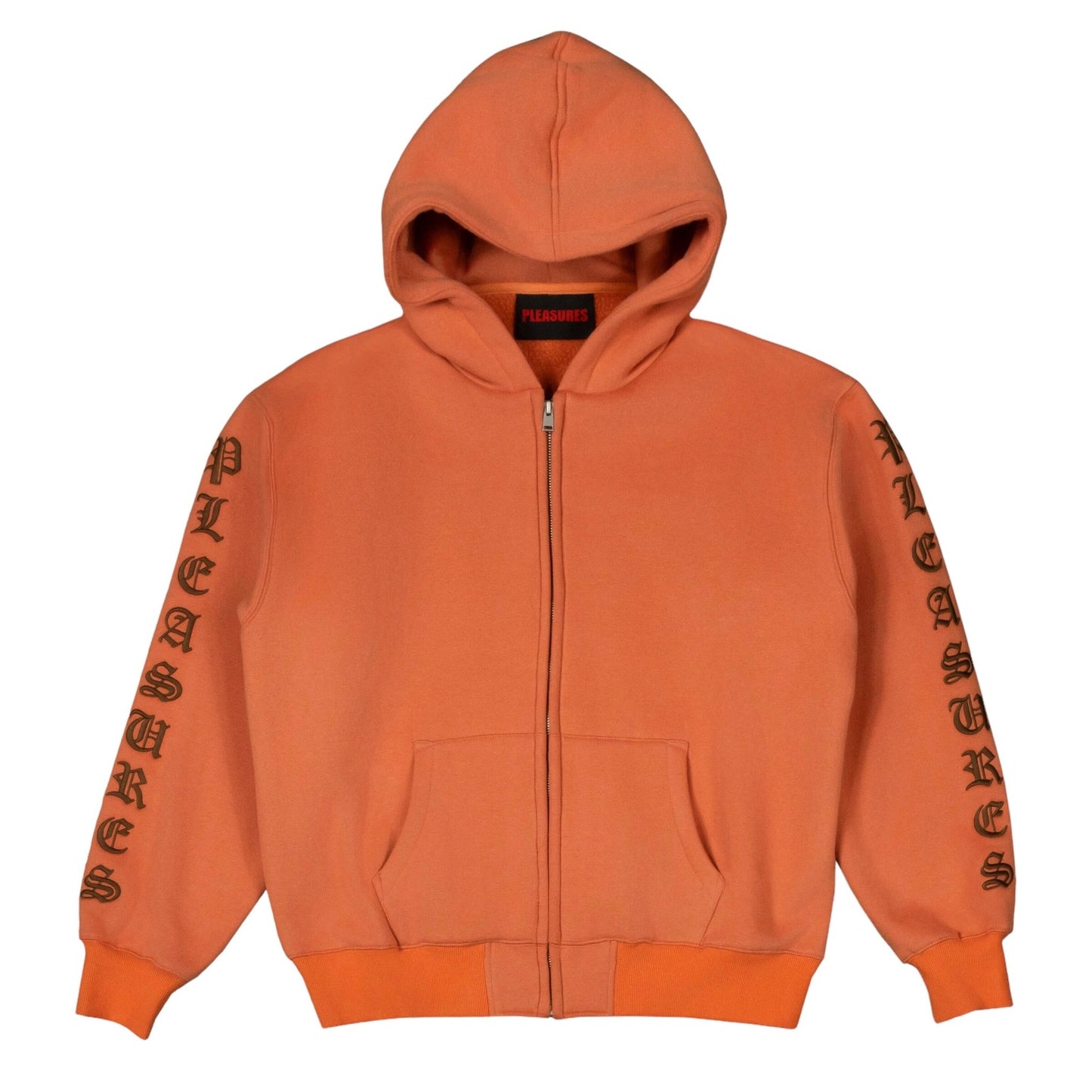 The PLEASURES OE ZIP UP HOODIE RUST is an orange, relaxed fit zip-up hoodie featuring "PLEASURES" printed on both sleeves. It's crafted from heavyweight cotton with a brushed fleece interior for extra comfort.