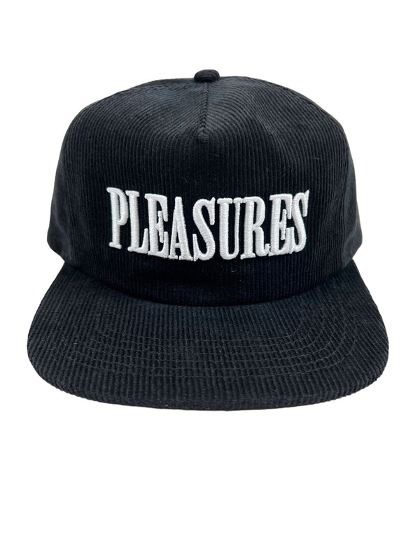 The PLEASURES ONYX CORDUROY SNAPBACK ONYX is a black corduroy hat featuring "PLEASURES" embroidered in large white letters on the front. It has a front panel with a flat, wide brim.