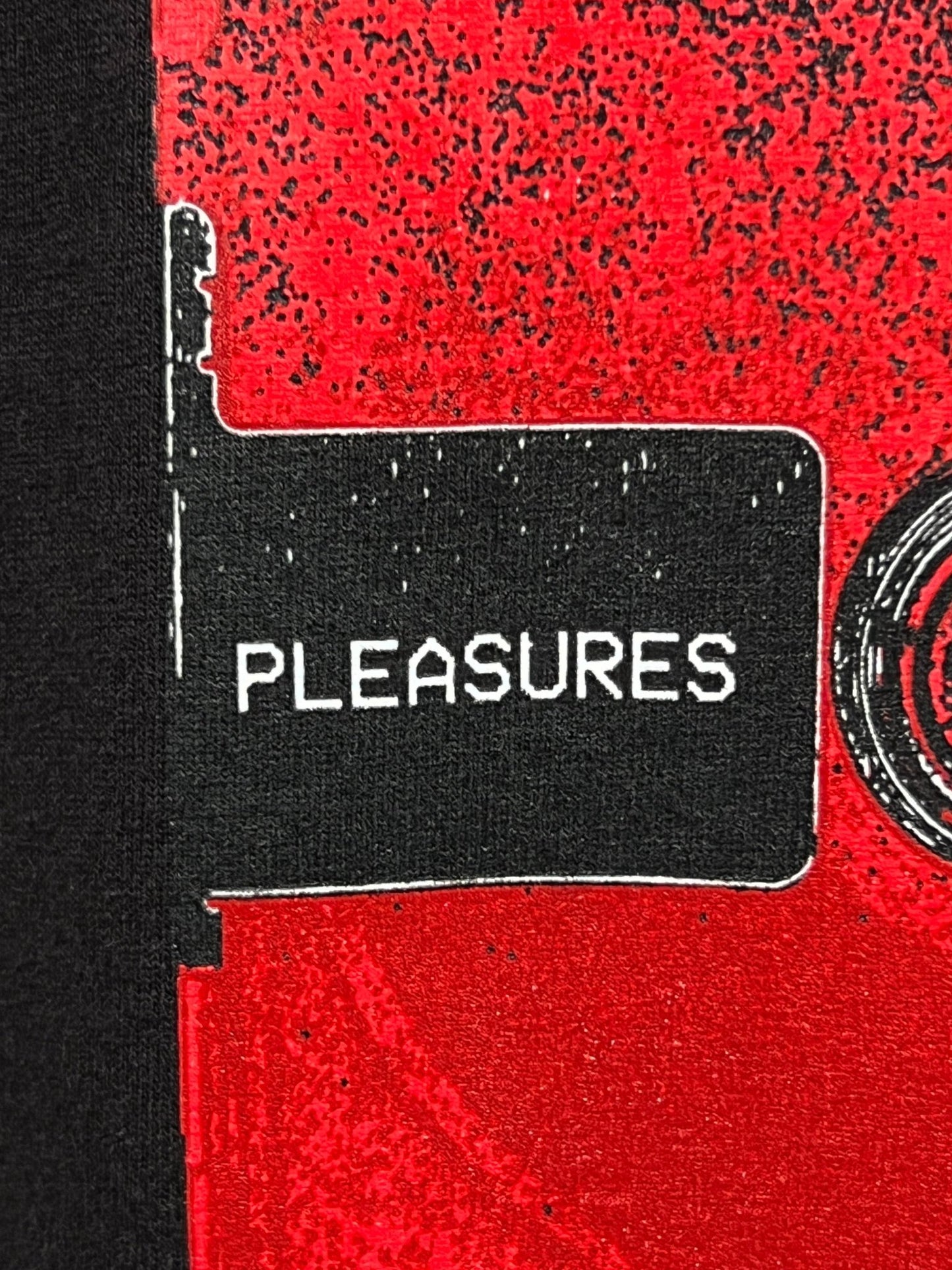 Close-up of a black sign with white text that reads "PLEASURES" against a red and black background, reminiscent of the classic aesthetic found on a PLEASURES OPERA T-SHIRT BLACK by PLEASURES.