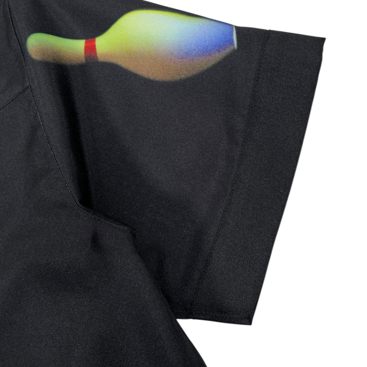 A close-up of the Pleasures Time Bowling Button Up Black by PLEASURES shows its soft polyester fabric and a vibrant bowling pin graphic on the sleeve.