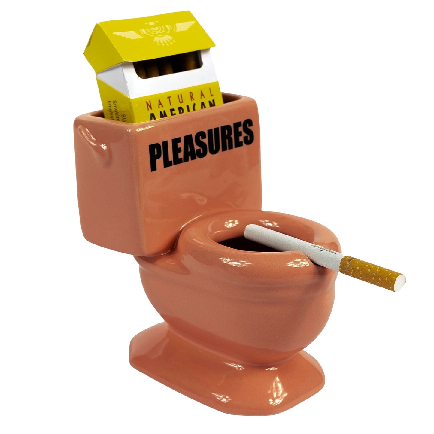 The PLEASURES TOILET ASHTRAY PINK by PLEASURES is a small ceramic ashtray shaped like a pink toilet, featuring a cigarette resting on the seat and a pack of "NATURAL AMERICAN PLEASURES" cigarettes tucked into the tank.