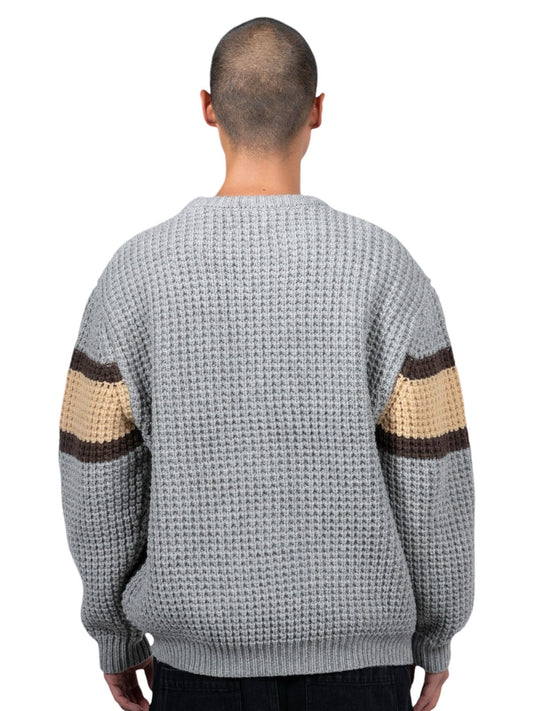 A person faces away wearing the Pleasures Twitch Chunky Knit Sweat Grey by PLEASURES, featuring brown and beige striped sleeves. With a shaved head, they add to the cozy vibe of this wool blend garment.