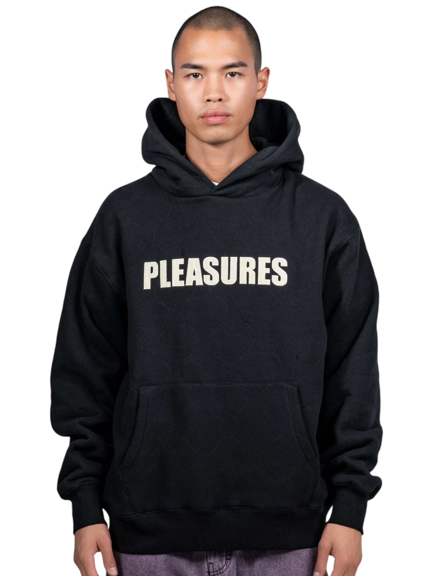 Against a plain white backdrop, a person wears the Pleasures Wave Quilted Hoodie Black by PLEASURES, featuring "Pleasures" prominently displayed on it.
