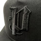 Close-up of the PURPLE BRAND A2054-TTGT224 black cotton twill trucker hat, featuring a raised, embroidered gothic-style "D" on the front.