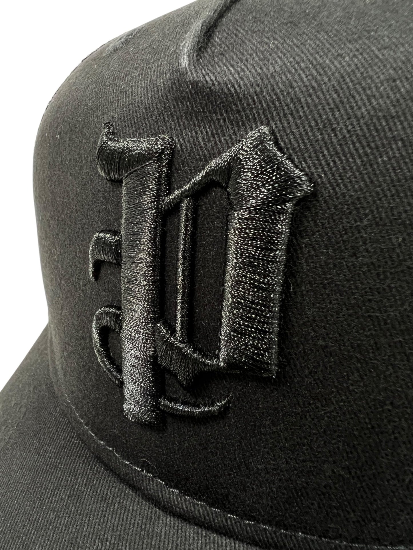 Close-up of the PURPLE BRAND A2054-TTGT224 black cotton twill trucker hat, featuring a raised, embroidered gothic-style "D" on the front.