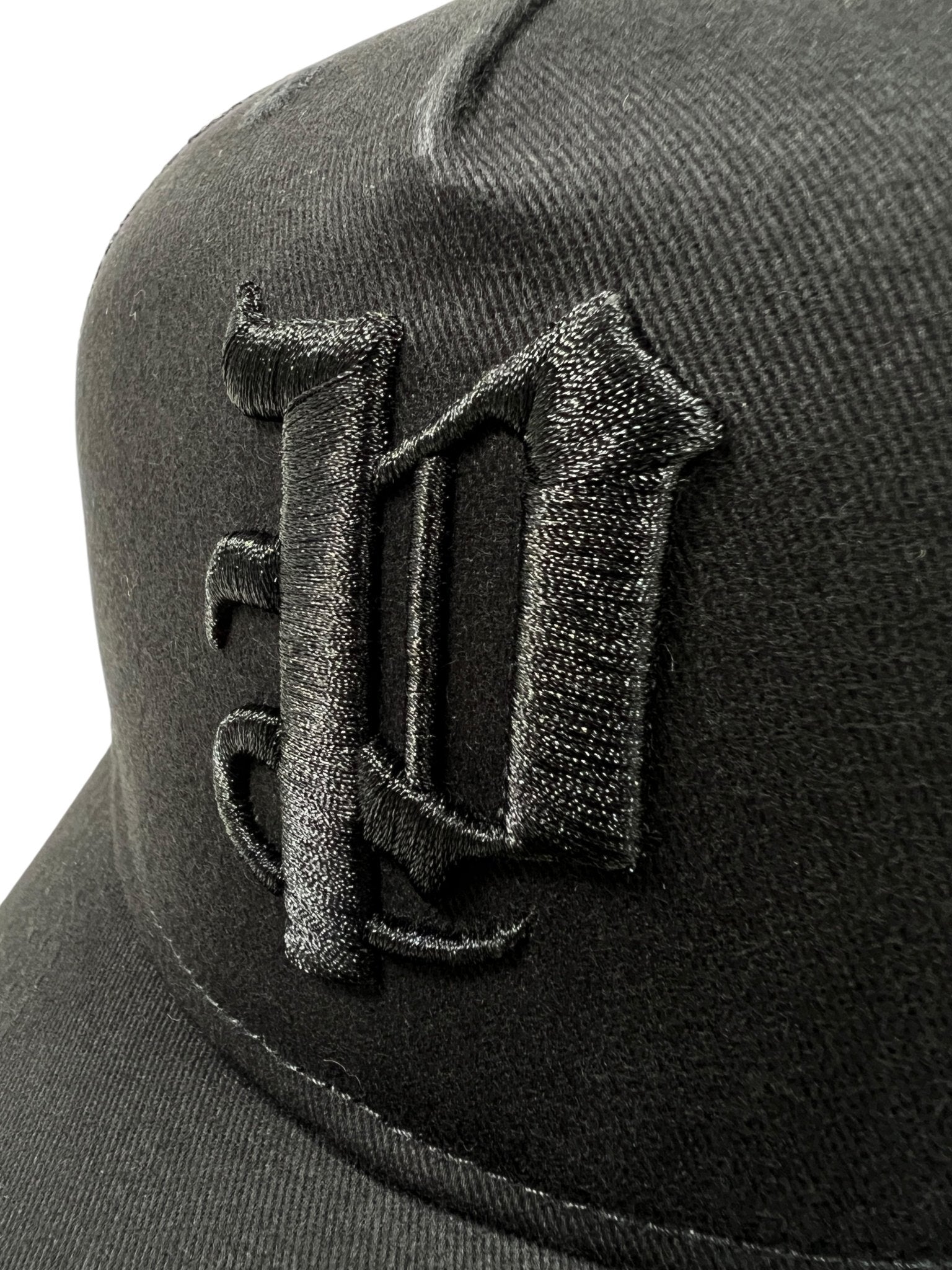 Close-up of the PURPLE BRAND A2054-TTGT224 black cotton twill trucker hat, featuring a raised, embroidered gothic-style "D" on the front.