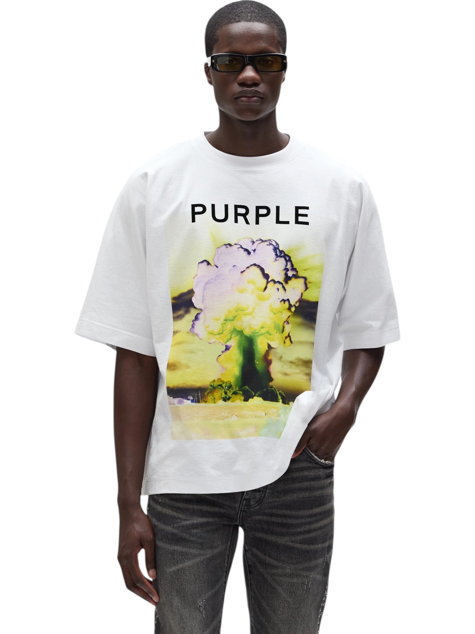 A man in sunglasses wears the PURPLE BRAND M1057-TWFM325 Textured Jersey Top in white, an oversized 100% cotton tee with "PURPLE" text and a digital explosion graphic, paired with dark jeans.