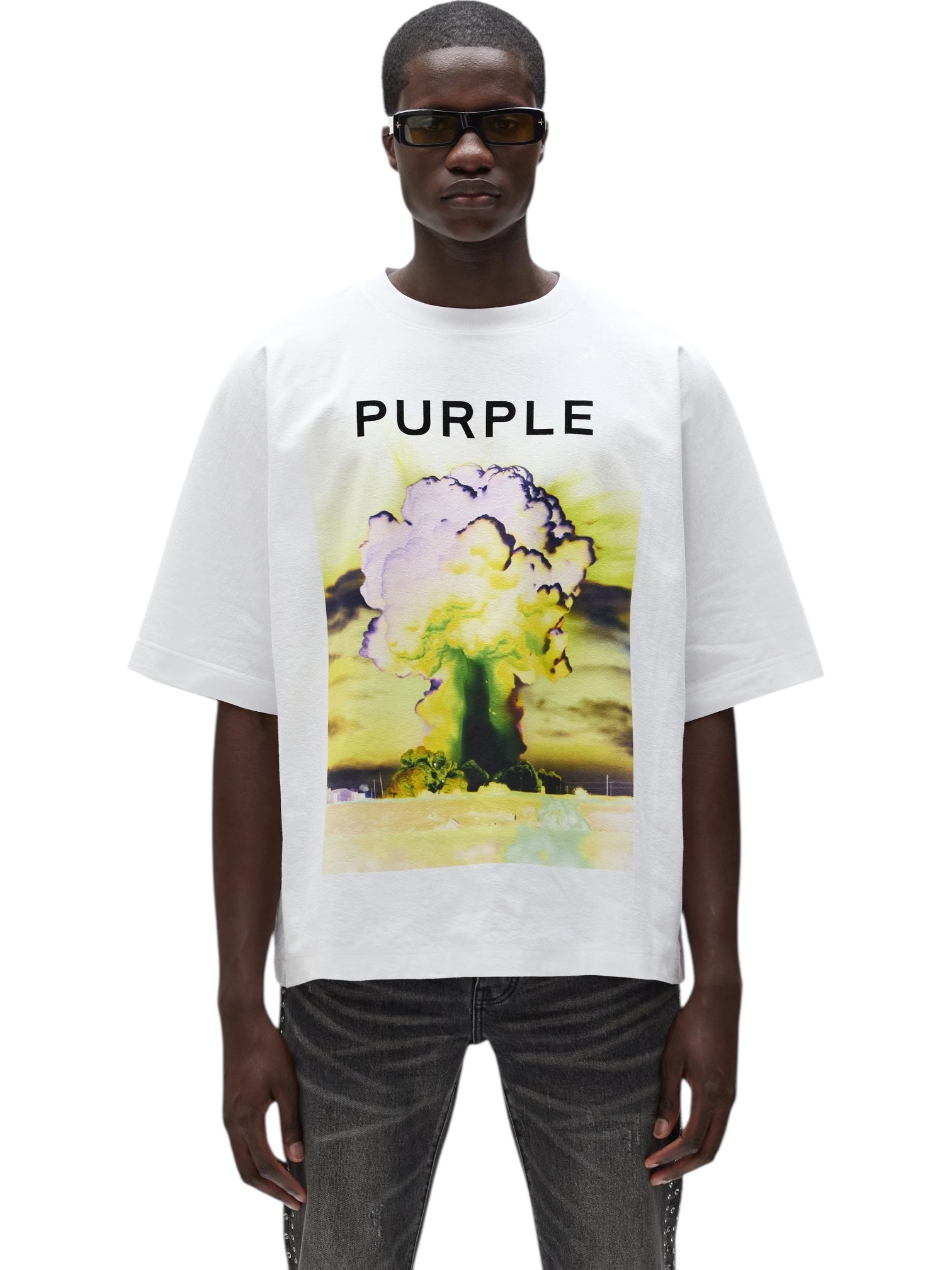 A person wearing sunglasses and a PURPLE BRAND M1057-TWFM325 Textured Jersey Top White, 100% cotton, featuring a digital graphic with "PURPLE" and a mushroom cloud explosion on the front.