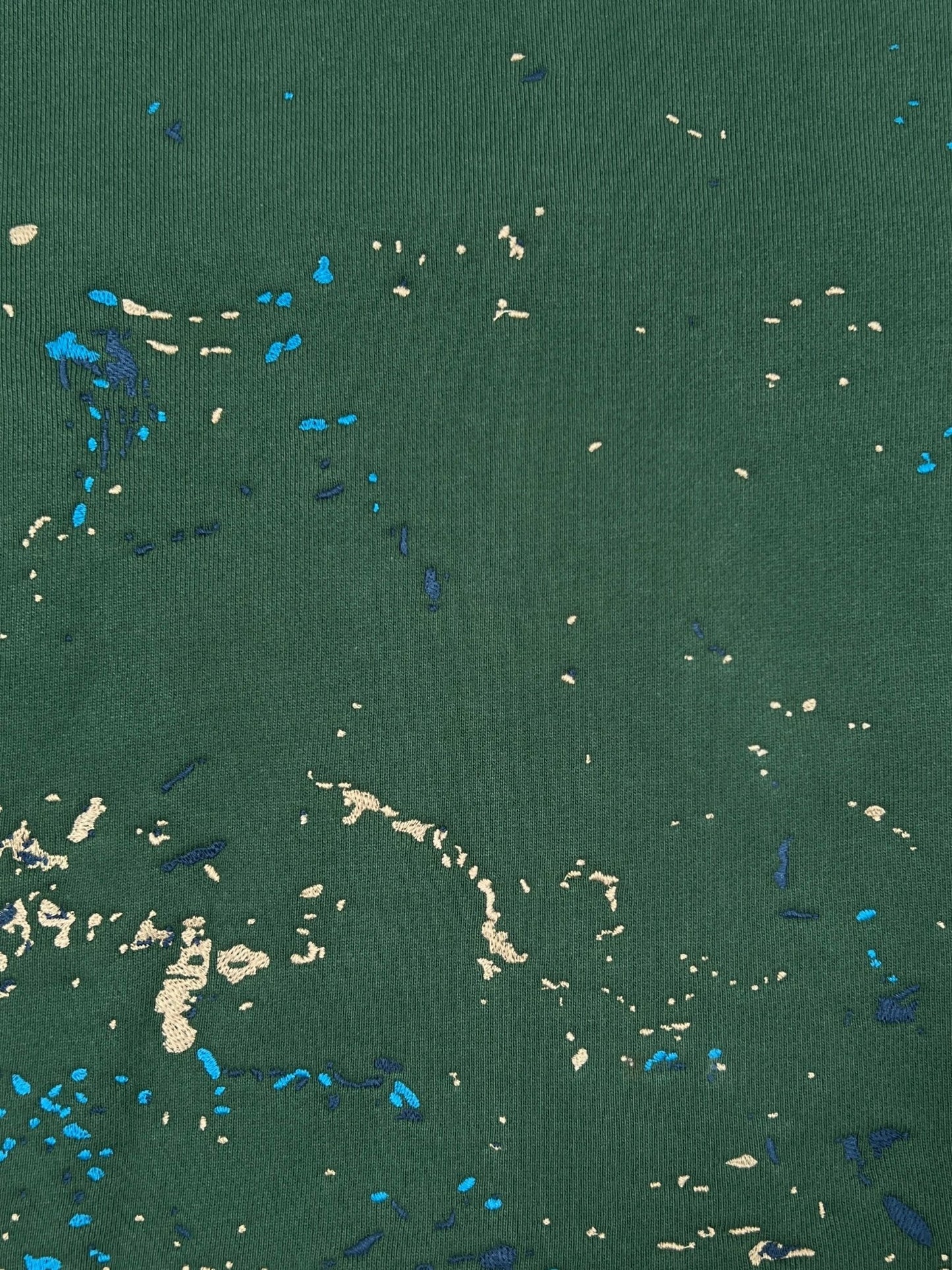 Close-up of the PURPLE BRAND M4104-HFGH425 Heavyweight Fleece Hoodie Green, showing its green fabric with unique beige and blue paint splatter details in a crackle print effect.