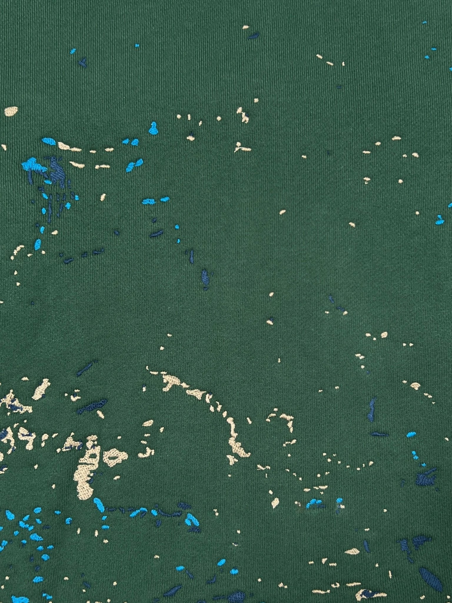 Close-up of the PURPLE BRAND M4104-HFGH425 Heavyweight Fleece Hoodie Green, showing its green fabric with unique beige and blue paint splatter details in a crackle print effect.