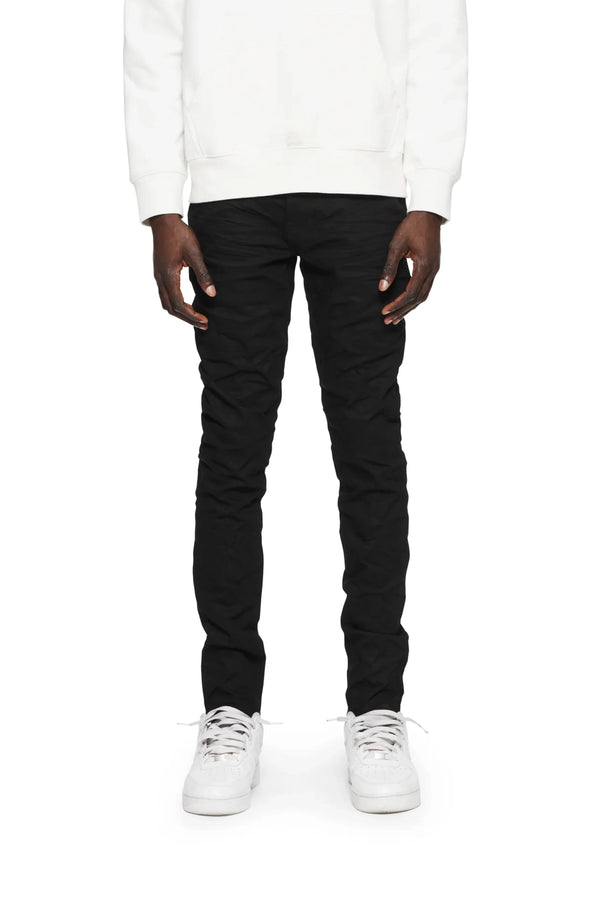 A person is wearing a white sweatshirt and PURPLE BRAND Purple Brand P001-BLKR Black Raw222 low-rise skinny pants, paired with white sneakers, standing with their hands at their sides.