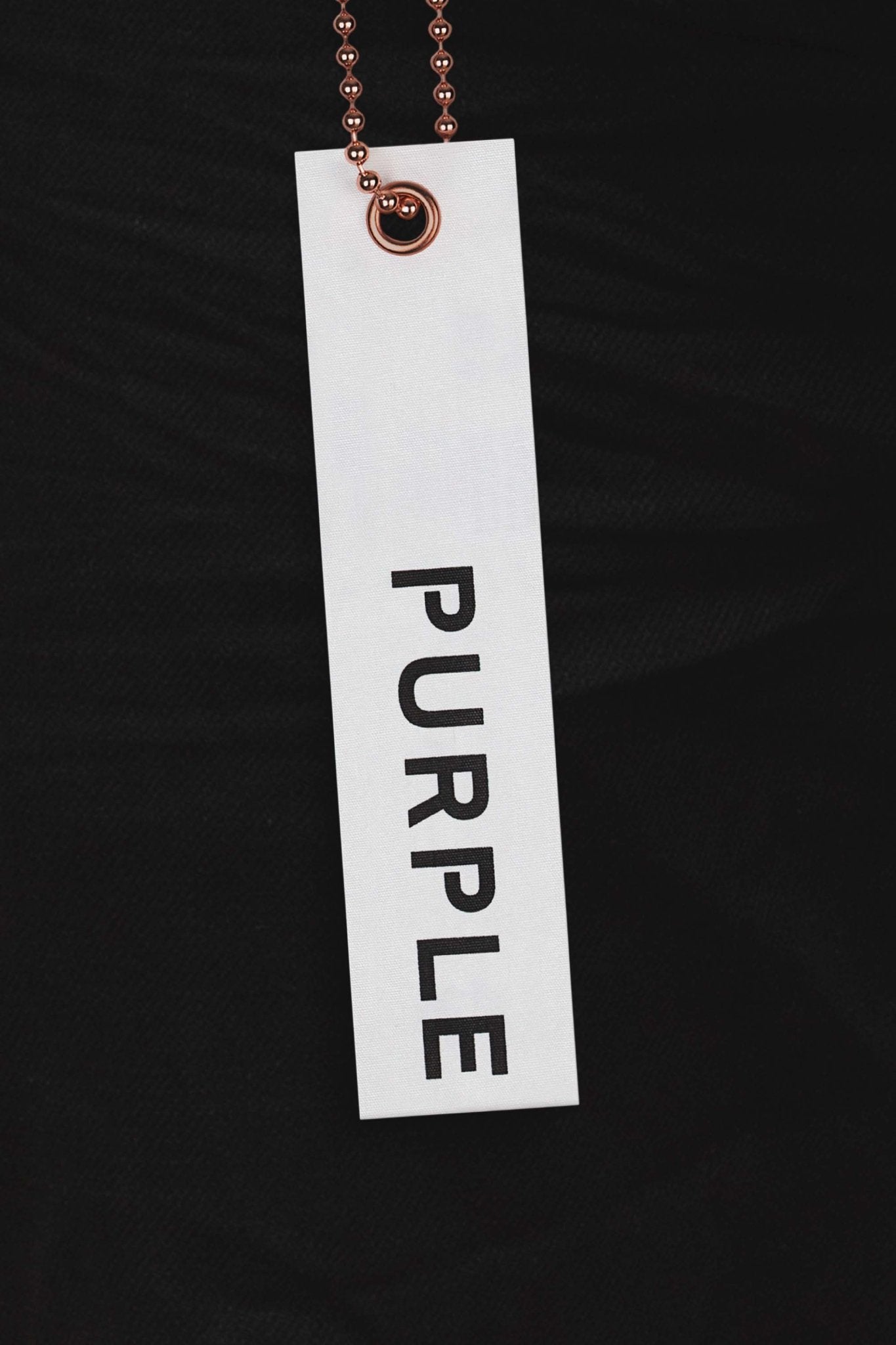 A tag with "PURPLE BRAND" printed in black letters hangs against the deep black color of the Purple Brand P001-BLKR Black Raw222, adding a sense of elegance and sophistication.