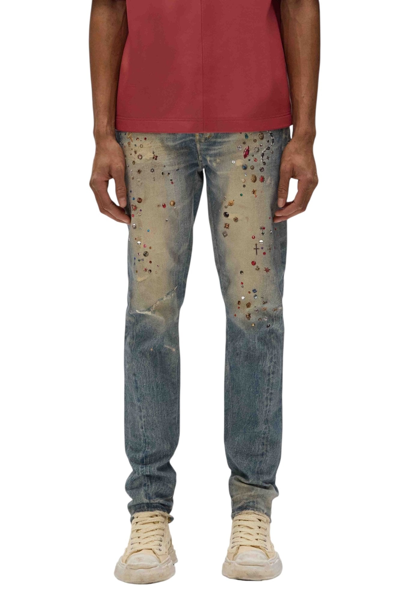 A person wearing a red shirt and the Purple Brand P001-CYWI Skinny Cyanine Jewel Indigo jeans, made from premium stretch denim with decorative patterns in light indigo, stands confidently against a white background, paired with crisp white sneakers.