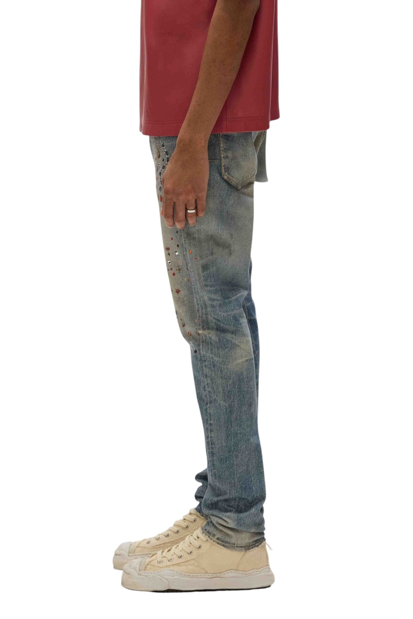 A person in a red shirt and light-colored high-top sneakers stands sideways, highlighting PURPLE BRAND's Purple Brand P001-CYWI Skinny Cyanine Jewel Indigo jeans.