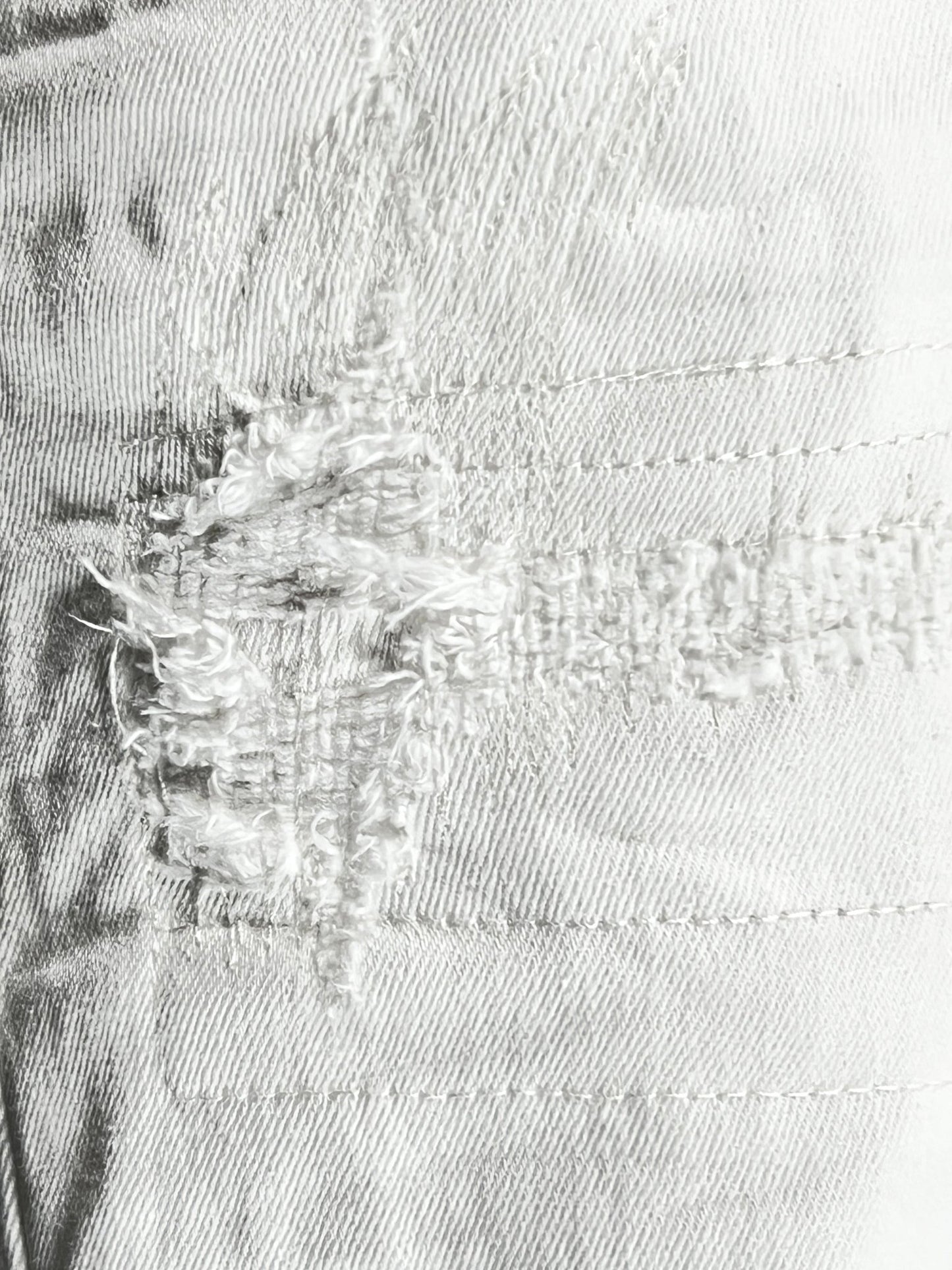 Close-up of a trendy PURPLE BRAND P001-LDWH LIGHT DESTROY WHITE denim fabric with frayed threads and visible stitching details.