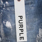 Close-up of a tag labeled "PURPLE BRAND" in bold black, attached to the Purple Brand P001-SAFC Angel Silver Foil Cross Indigo denim, highlighting unique washes and dyes for a speckled, weathered look.